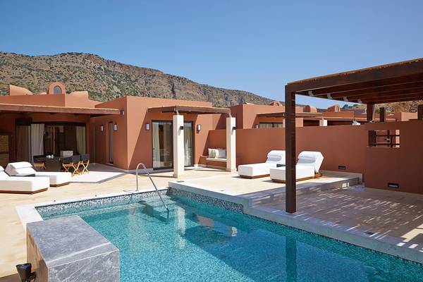 Außenbereich des Domes of Elounda, Autograph Collection mit Pool, Liegestühlen und Panoramablick auf Berge