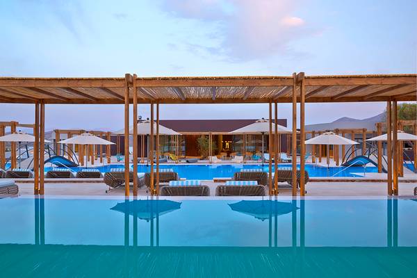Außenpoolbereich des Domes of Elounda Hotels mit Holzpergola und Sonnenschirmen.