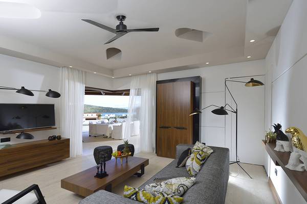 Innenansicht des Wohnzimmers im Domes of Elounda mit grauem Sofa, Holztisch und weißen Vorhängen.