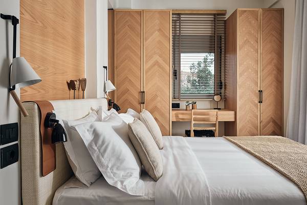 Schlafzimmer im Domes of Elounda, Autograph Collection mit Bett, Holzmöbeln und Fenstern.