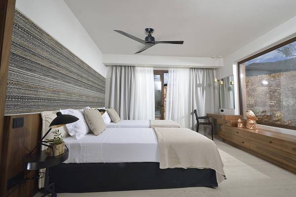 Schlafzimmer im Domes of Elounda, Autograph Collection mit zwei Betten, Deckenventilator und Steinmauer im Hintergrund.