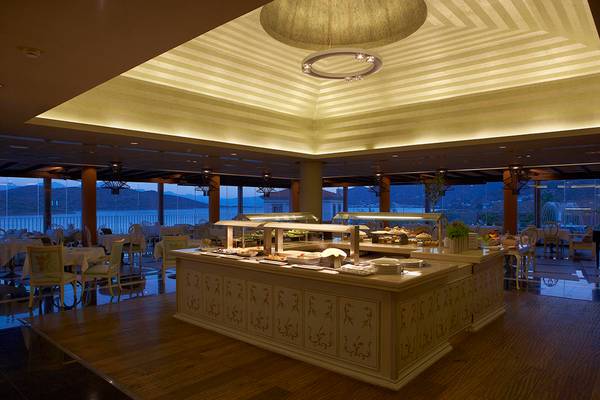 Innenansicht des Speisesaals im Domes of Elounda, Autograph Collection mit offenem Buffet, Tischen und Stühlen sowie großen Fenstern.