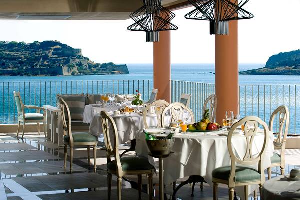 Terrasse mit Meerblick im Domes of Elounda, Autograph Collection mit gedeckten Tischen und Früchten.