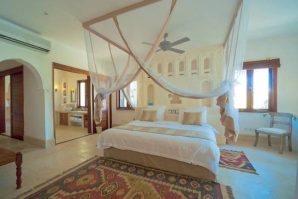 Schlafzimmer des Swahili Beach Resorts mit einem großen Bett, Moskitonetz, Teppich und offenem Badezimmer.