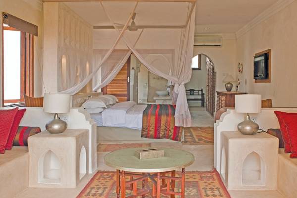 Schlafzimmer im Swahili Beach Resort mit einem Bett, Vorhängen, Nachttischen und Lampen.