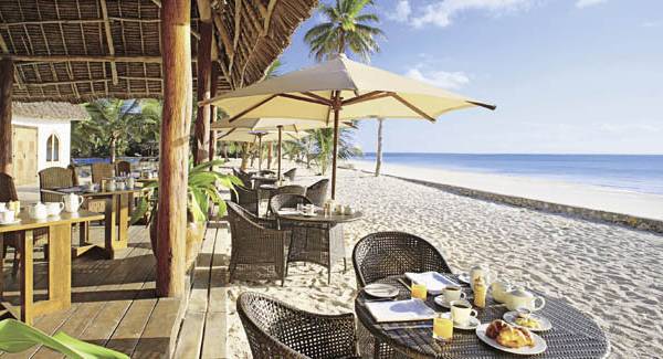 Strandrestaurant des Sultan Sands Island Resorts mit Tischen und Stühlen im Freien und einem großen Sonnenschirm.