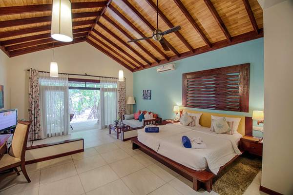 Innenansicht eines Doppelzimmers im Robinson Maldives mit Bett, Schreibtisch und Wohnzimmerbereich.