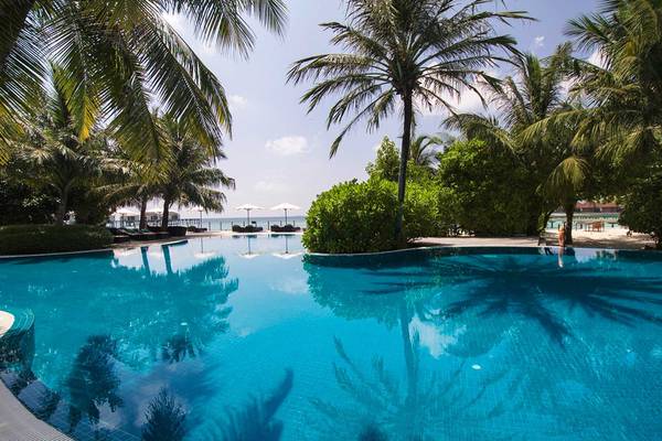 Außenpool des Robinson Maldives Hotels im Sommer mit Palmen und Strand im Hintergrund.