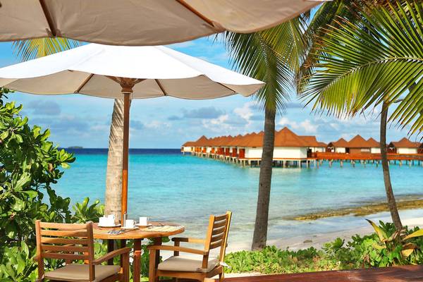 Terrasse des Robinson Maldives Hotels mit Tisch, Umbrella und Blick auf die Wasserbungalows und den Ozean.