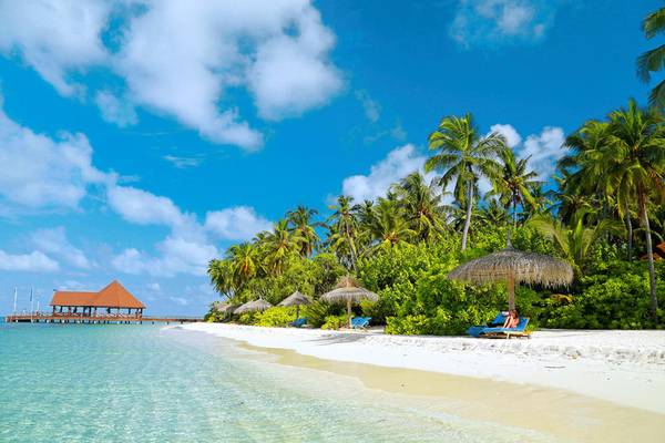 Strand des Robinson Maldives mit Sonnenliegen, Palmen und einem Pavillon am Wasser