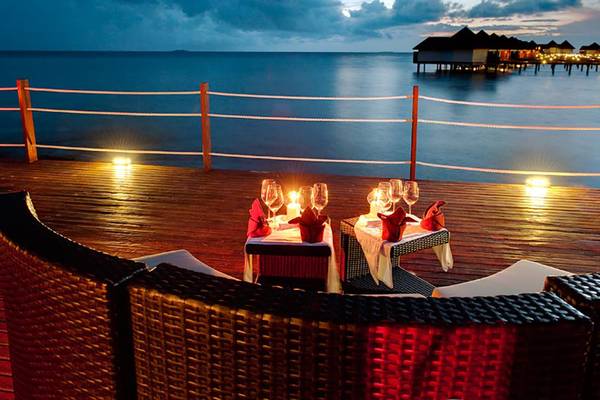 Abendessen auf Holzdeck im Robinson Maldives mit Blick auf das Meer und beleuchtete Hütten