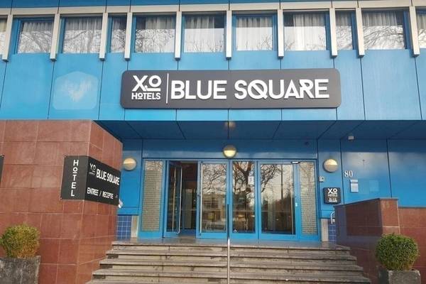 Eingangsbereich des XO Hotels Blue Square mit zwei Pflanzkübeln und Treppen.