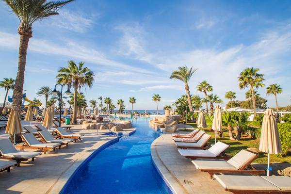 Pool-Loungebereich im Adams Beach Hotel mit Sonnenliegen und Palmen