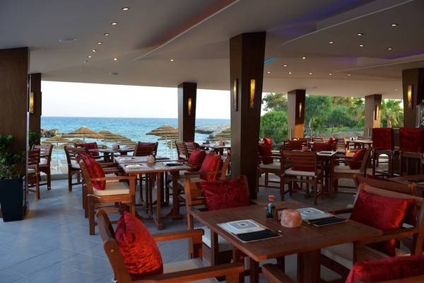 Innenansicht des Restaurants im Adams Beach Hotel mit Blick auf das Meer und Sonnenschirme.