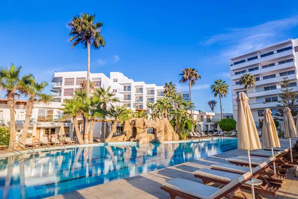 Außenbereich des Adams Beach Hotels mit Pool, Liegestühlen und Palmen