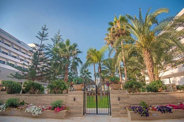 Eingang des Adams Beach Hotels mit geschwungenen Toren und üppiger Gartenanlage.
