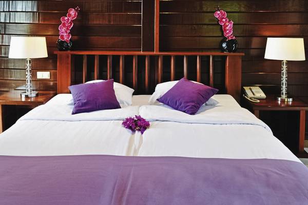 Hotelzimmer im Van der Valk Kontiki Beach Resort Curaçao mit zwei Betten, weißen Laken, violetten Kissen und Blumendekor.