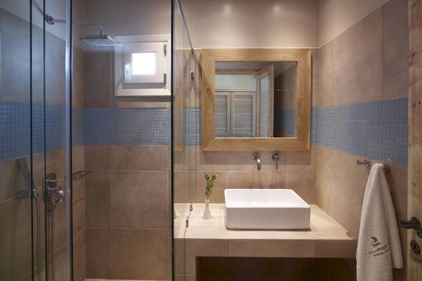 Badezimmer im Vencia Boutique Hotel mit Glasdusche, Waschbecken und beigen Fliesen.