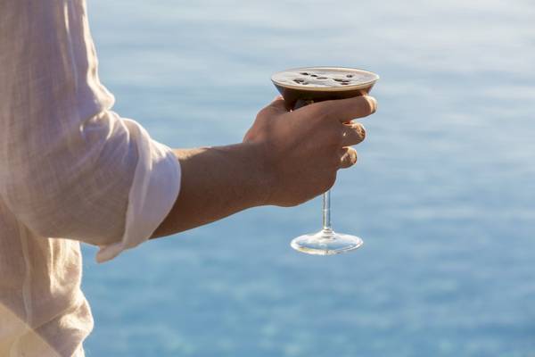 Hand, das ein Cocktailglas am Meer hält