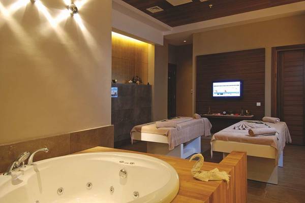 Massageraum im Commodore Elite Suites & Spa mit Badewanne, Massageliegen und Fernseher.