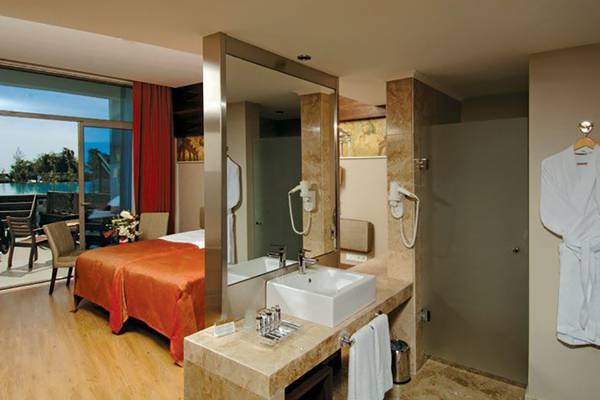 Badezimmer des Commodore Elite Suites & Spa mit Blick auf den Ozean, Bett, Spiegel, Waschbecken und Bademänteln.