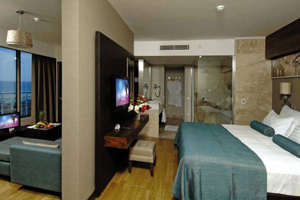 Innenansicht eines Hotelzimmers im Commodore Elite Suites & Spa mit einem Bett, Fernseher, Tisch und Meerblick.