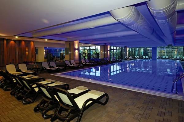 Innenpool im Commodore Elite Suites & Spa mit vielen Liegestühlen und blauer Beleuchtung.