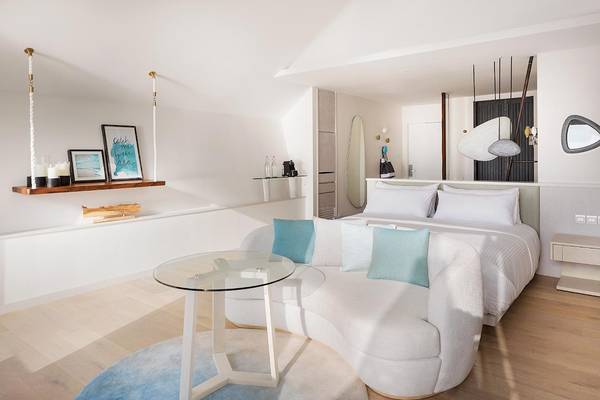 Innenansicht des Schlafzimmers im LUX South Ari Atoll Hotel mit einem großen Bett, weißen Möbeln und einem Glastisch.
