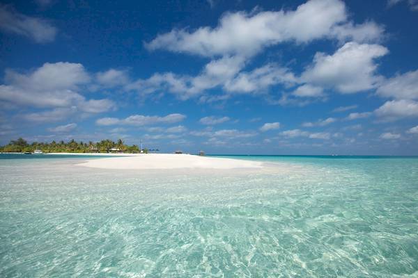 Ein Bild des LUX South Ari Atoll Hotels zeigt eine Insel mit klarem Wasser unter einem blauen Himmel