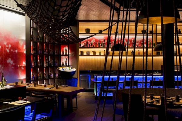 Innenansicht der Bar im LUX South Ari Atoll Hotel mit dekorierten Regalen, blau beleuchteter Theke und stimmungsvoller Beleuchtung.