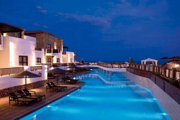 Nachtansicht des Poolbereichs des Costa Lindia Beach Resorts mit Lounge-Stühlen und Sonnenschirmen