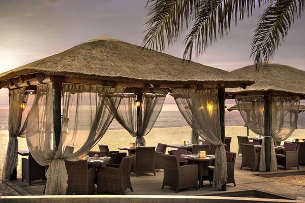 Außenrestaurant am Strand des Fujairah Rotana Resorts mit überdachten Tischen und Stühlen.