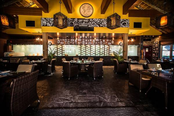 Innenansicht des Fujairah Rotana Resort & Spa Best Fresh Seafood Restaurants mit gelben Wänden, Holzbalken und vielen Tischen und Stühlen.