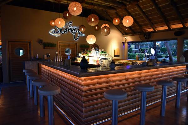 Innenansicht der Sharkey Bar im Fujairah Rotana Resort & Spa mit Holztheke und Barhockern.