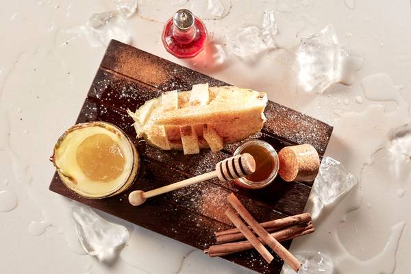 Avra Imperial Essenz Cocktail auf einem Holzbrett mit Eiswürfeln, Zimtstangen und Honig.