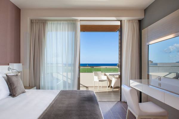 Innenansicht eines Zimmers im Avra Imperial Hotel mit Blick auf einen Balkon und das Meer.