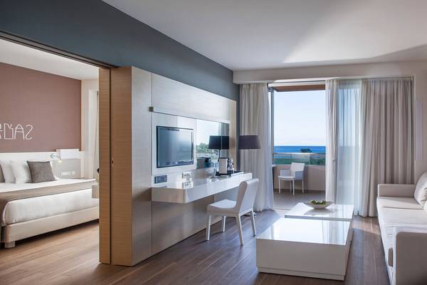 Innenansicht einer Suite im Avra Imperial Hotel mit einem Bett, Schreibtisch und Meerblick.