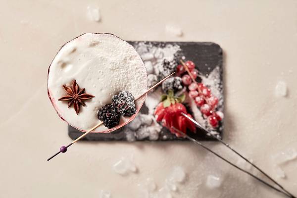 Ein Cocktail mit weißer Creme, Zimt und Beeren auf einem schwarzen Teller.