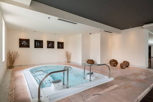 Innenbereich des Avra Imperial Hotels mit Whirlpool, umgeben von weißen Wänden und Holzboden.
