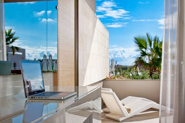 Ein Laptop auf einem Balkon mit Ausblick auf eine sonnige Landschaft und blauem Himmel.