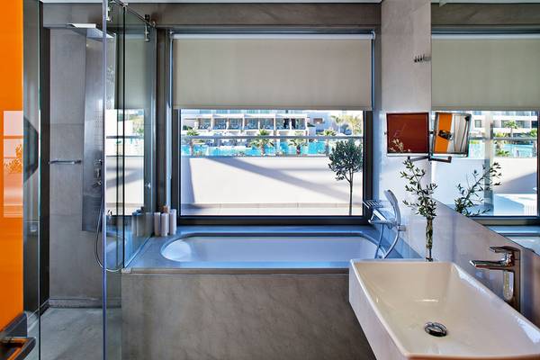 Badezimmer im Avra Imperial Hotel mit Badewanne, Regendusche und Ausblick auf den Pool.