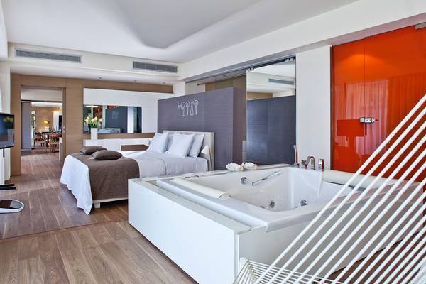 Luxuriöses Schlafzimmer im Avra Imperial Hotel mit Bett, Badewanne und Fernseher.