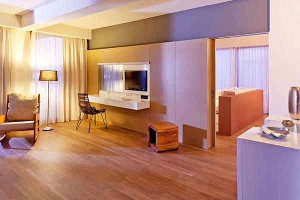 Innenansicht eines Zimmers im Avra Imperial Hotel mit Holzboden, moderner Einrichtung und Fernseher.