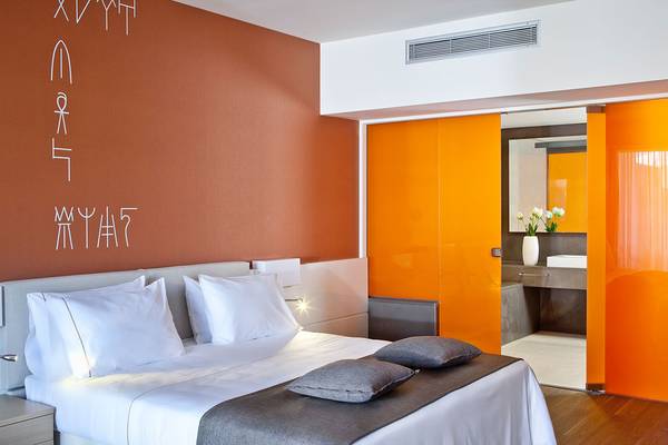 Schlafzimmer im Avra Imperial Hotel mit einem Bett, Kissen und einem orangefarbenen Wanddesign.