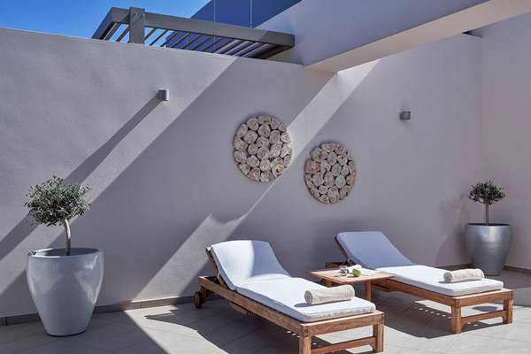 Terrasse im Avra Imperial Hotel mit zwei Lounge-Sesseln, Pflanzen und Wandkunst.
