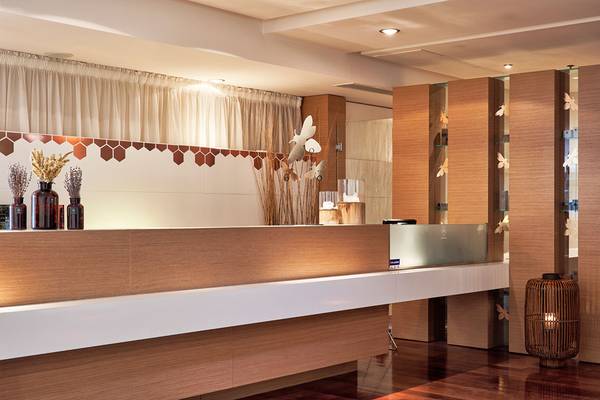 Empfangsbereich des Avra Imperial Hotels mit Holzwand und Empfangstresen.