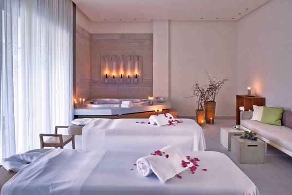 Spa-Behandlungsraum im Avra Imperial Hotel mit zwei Massageliegen, einem Whirlpool und dekorativen Kerzen.