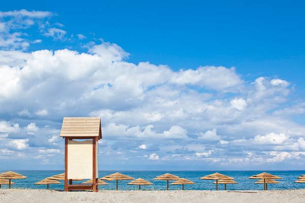 Strand mit Sonnenhutchen unter bewoelkter Himmel, mehrere Strohhutchen am Strand