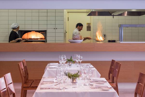 Restaurantszene im Avra Imperial Hotel mit Koch, der Flammen erzeugt, und Kellnerin hinter Ofen