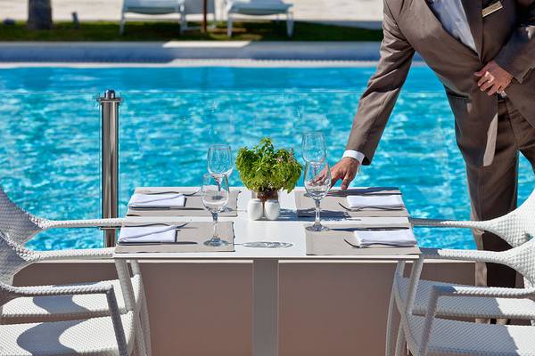 Mann im Anzug, der einen Tisch im Avra Imperial Hotel am Pool serviert